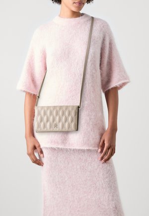 Roze donzige gebreide top gecombineerd met een beige gewatteerde schoudertas, met een kenmerkend logo-detail en een lange schouderband. Zachte texturen zijn prominent aanwezig.