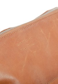 Pochette en cuir marron avec une texture lisse et un léger éclat. Dotée d'une fermeture éclair en argent et d'un détail de couture visible d'un côté.