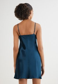 Satin kinesisk klänning i djup teal, med tunna justerbara axelband, en rak silhuett och en mjuk struktur med en subtil glans.