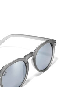 Šedé, průhledné sluneční brýle s kulatými čočkami, které mají jedinečný, úhlový design rámu a zrcadlové čočky. Akcentované minimalním logem.