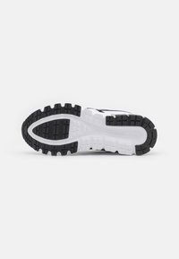 Sole di scarpa sportiva in bianco e nero con gomma texture, scanalature profonde per la trazione e una sezione centrale liscia.