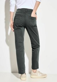 Pantalones de algodón verdes con pierna recta y dos bolsillos traseros, combinados con zapatillas beige. La tela tiene una textura suave y un diseño minimalista.