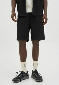 Black ribbed shorts with side pockets, paired with a white ribbed top and cream socks featuring text, completed with black athletic shoes.