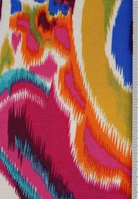 Gros plan sur un tissu coloré avec des motifs abstraits en zigzag rose, orange, bleu, jaune, vert et blanc, à côté d’une échelle de mesure sur la droite.