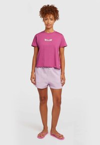 Pink cropped t-shirt with floral text design, paired with light purple drawstring shorts and pink flip-flops. Smooth cotton materials.