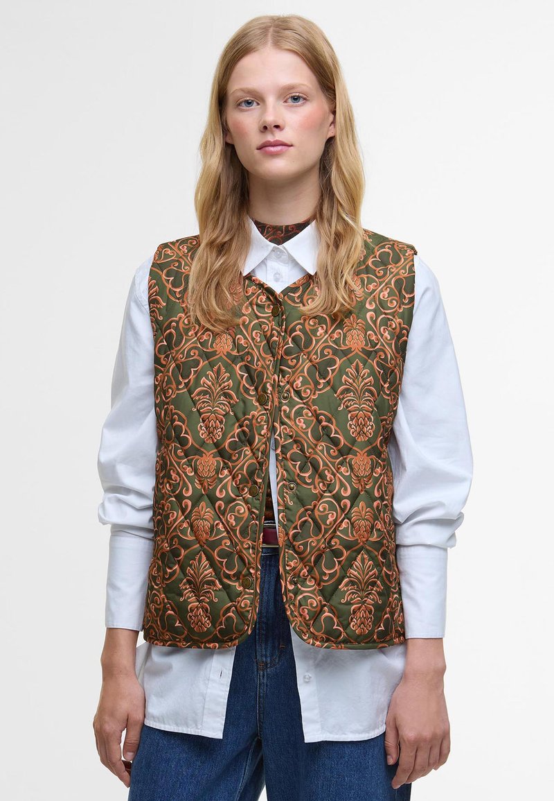 Quilted vest in green fabric with ornate orange floral pattern. Features a rounded neckline, button closure, and layered under a white shirt.