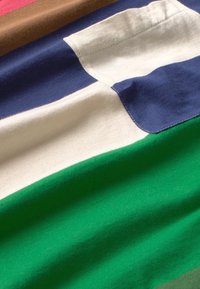 Multicolored fabric featuring brown, navy, cream, and green stripes; soft texture with visible stitching and a rectangular patch detail.