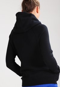 Schwarzes Kapuzen-Sweatshirt mit lockerer Passform, weicher Textur und gerippten Bündchen. Es verfügt über eine große, gemütliche Kapuze und ein nahtloses Schulterdesign.