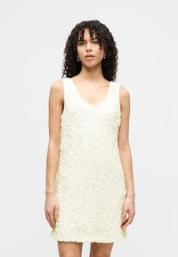 Αμάνικο, φόρεμα μήκους μέχρι το γόνατο σε απαλό ελεφαντόδοντο με υφασμάτινη, διακοσμητική εφαρμογή με μοτίβα λουλουδιών. Στρογγυλή λαιμόκοψη και ίσια σιλουέτα.