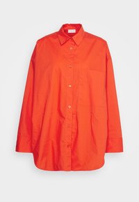 Chemise orange vif à manches longues avec boutons, col et poche poitrine, présentée à plat sur un fond blanc uni.