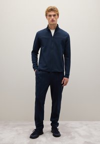 Completo sportivo navy realizzato in tessuto leggero, composto da una giacca con zip, maniche lunghe e pantaloni aderenti con polsini elasticizzati.