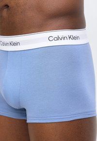 Κοντινό πλάνο ενός ατόμου που φοράει ανοιχτομπλε βαμβακερά εσώρουχα Calvin Klein με λευκή μέση που φέρει το όνομα της μάρκας σε μαύρο κείμενο.