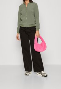 Grön bomberjacka med dragkedja, svarta vida byxor, silverfärgade sneakers och en fluffig rosa handväska med ett böjt handtag.