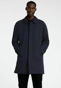 Mornarski plašč z gumbastim zapiranjem, stranskimi žepi in ovratnikom. Izdelan iz gladkega, trpežnega materiala z elegantno silhueto.