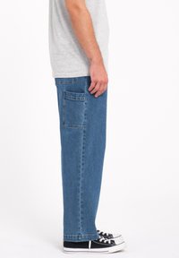 Jeans in denim azzurro con vestibilità dritta, dotati di tasca posteriore e dettagli cuciti. Abbinati a sneakers nere.