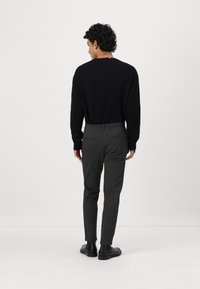Svart strikket genser, grå skreddersydde bukser med elastisk liv, glatt tekstur og ankle-lengde, kombinert med svarte sko.