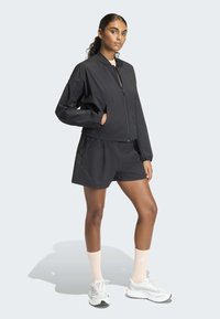 Fekete könnyű bomberdzseki cipzáras zárral és két oldalzsebbel, fekete rövidnadrággal és fehér sportcipővel rózsaszín zoknival párosítva.