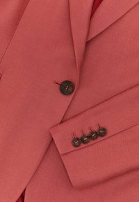 Gros plan d'un blazer texturé rose avec un bouton devant et quatre boutons sur le poignet de la manche.