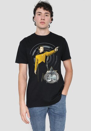 Black cotton T-shirt featuring a yellow uniform design with a character holding a device, surrounded by a circular graphic and text.