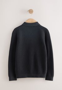 Pull en maille noire à surface texturée, col, poignets et ourlet côtelés. Présenté suspendu sur un cintre en bois devant un fond clair.
