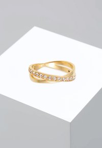 Anello d'oro con bande intrecciate, caratterizzato da una fila di pietre trasparenti su un lato, texture liscia e finitura lucida.