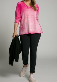 Růžový dlouhý rukáv s přechodem barev a V-výstřihem s texturovaným povrchem, doplněný černými kalhotami a světlými teniskami. V ruce drží černý kardigan.