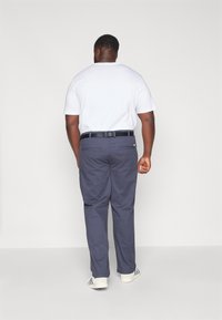 Marineblaue Hose mit geradem Schnitt und zwei Gesäßtaschen, getragen mit einem schlichten weißen T-Shirt und einem schwarzen Gürtel, von hinten betrachtet.