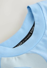 T-shirt en coton bleu clair avec un col rond. Présente une texture lisse et une étiquette noire à l'intérieur avec un texte blanc indiquant "Ted Baker".