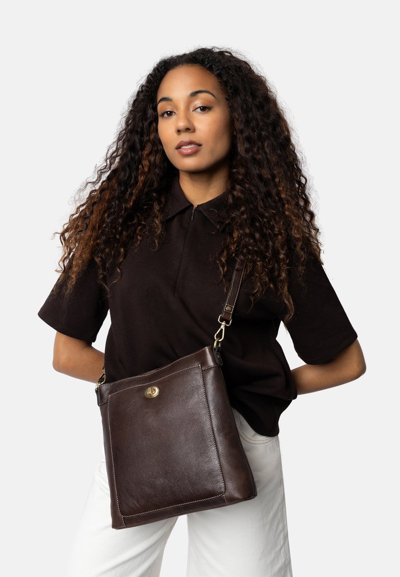Borsa a spalla in pelle marrone con una superficie liscia, forma quadrata, dettagli in hardware dorato e tracolla regolabile.