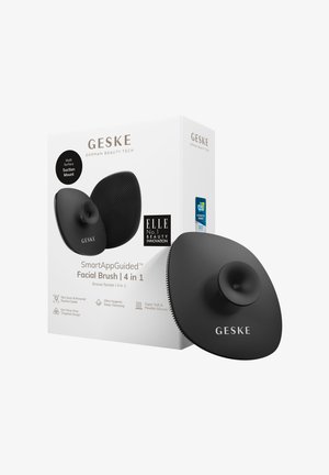 Svart silikonansiktsborste med sugfäste; har en texturerad yta; förpackad i en vit låda med varumärke och produktinformation.