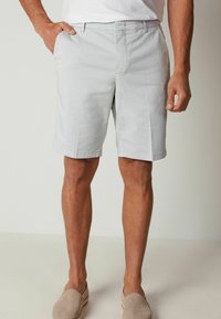 Shorts grigi chiaro realizzati in tessuto misto cotone, con tasche laterali, una linea dritta e una texture liscia. Indossati con scarpe beige senza lacci.