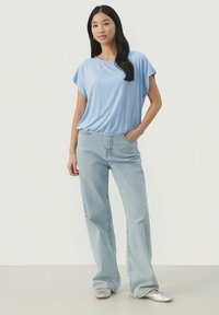 Lyseblå kortærmet top med løs pasform, parret med højtaljede lys denim jeans. Har en samlet kant og sølv flade sko.
