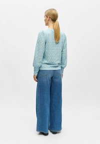 Lys blå strukturert genser med puffede ermer, kombinert med vide jeans. Antrekket har en avslappet, ledig passform.