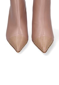 Stivaletti beige in pelle con punta affilata e decorazioni in borchie dorate sulla parte della punta, mostrati frontalmente su uno sfondo bianco.