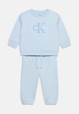 Világoskék hosszú ujjú pulóver és hozzáillő nadrág szett, a mellrészen "cK Calvin Klein" logóval, valamint elasztikus mandzsettákkal az ujjakon és a nadrágon.