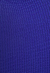 Tecido roxo texturizado com um padrão de ondas, apresentando uma fina estria que cria uma aparência dimensional. Material suave e flexível.