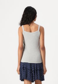 Canottiera grigia a costine con spalline larghe, indossata con una gonna a rouches a pois blu navy. Il tessuto sembra morbido e aderente.