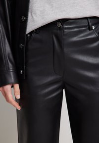 Melni ādas bikses ar gludu tekstūru, priekšējām kabatām un sudraba apdari pie jostas. Stilizētas ar pelēku augšdaļu.