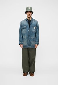 Τζιν μπουφάν με τέσσερις τσέπες και κλείσιμο με κουμπιά, σε συνδυασμό με χακί παντελόνι φαρδιάς γραμμής και ανοιχτοπράσινο καπέλο τύπου bucket. Καφέ παπούτσια.