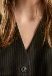 Schwarze Nadelstreifen-Weste mit tiefem V-Ausschnitt und einem einzigen runden schwarzen Knopf auf der Vorderseite. Glatte Stoffstruktur und taillierte Passform.