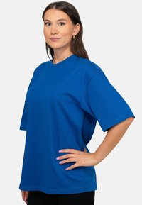 Maglietta over-size in cotone blu con maniche corte, scollo rotondo e spacchi laterali. Presenta cuciture minimali e una texture liscia.