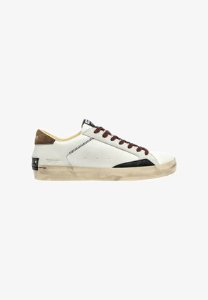 Sneaker bianca con accenti in suede marrone, dettagli in gomma scura, lacci marroni e suola testurizzata. Finitura usurata sulla punta e sulla suola.