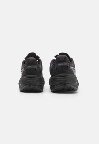 Chaussures de sport noires avec une tige en mesh, des détails texturés, une languette de traction et une semelle extérieure en caoutchouc durable, présentant un motif de crampons conséquent.