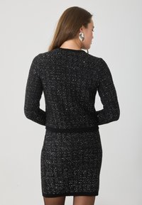 Čierne pletené šaty s textúrovaným vzorom, dlhými rukávmi, priliehavým pásom a rebrovaným lemom. Zvýraznené kovovými vláknami.