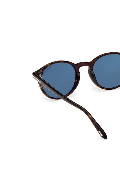 Occhiali da sole rotondi in tartaruga con lenti blu scuro e aste sottili, mostrati leggermente di lato su sfondo bianco.