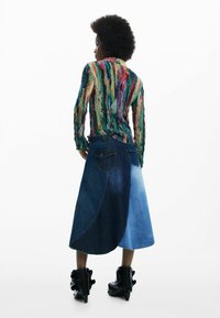 Top cu mâneci lungi din paiete multicolore, asortat cu o fustă din denim cu design color-block în diferite nuanțe de albastru. Purtați cu cizme negre cu toc.