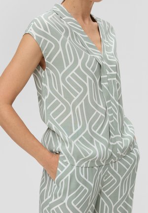 Mouwloze mintgroene top en broek met wit geometrisch patroon gedragen door persoon met handen in de zakken.