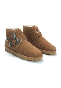 Botas de tobillo de ante marrón con dos correas ajustables que cuentan con hebillas metálicas. Forro interior suave, suela de goma plana y diseño de punta redondeada.