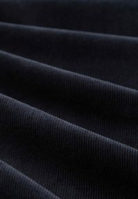 Mörk marinblå corduroytyg med en distinkt ribbad textur; vecken skapar ett vågigt mönster som framhäver djup och mjukhet.