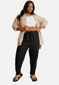 Beżowa koszula zapinana na guziki noszona na białym topie crop, w zestawieniu z czarnymi spodniami na gumkę i beżowymi sandałami. Gładkie tekstury z luźnym krojem.